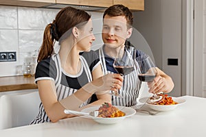 Valentine day romantic dinner at home. Happy couple smiling, clinking glasses and eating pasta with wine at kitchen