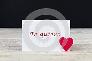 Valentine greeting card on wooden table with text written in spanish Te quiero, which means I love you. photo