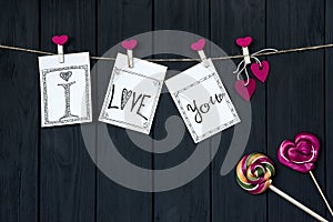Valentine`s card with a message `I love you` cord and pink pins with caramel hearts, hanging on texture background.