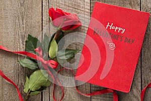 Valentine`s card. Red rose and red notebook with wishes on wooden board.