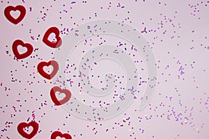 Valentine\'s concept with red hearts over the pink glitter on a pink background.