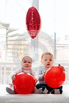 Valentine`s day. Baby boy and baby girl sitting in a crib with red balls in their hands. Vertical orientation
