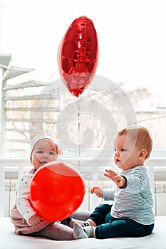 Valentine`s day. Baby boy and baby girl sitting in a crib with red balls. Vertical orientation