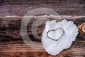 Valentine's Day background. Brown old winter wooden natural boards in with white heart made of snow. Top view.