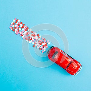 Valentine\'s Day background February 14th. Red retro toy car  red  pink  white hearts confetti  on blue background.