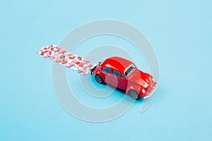 Valentine\'s Day background February 14th. Red retro toy car  red  pink  white hearts confetti  on blue background.