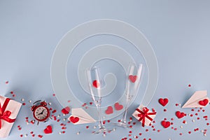 Valentine`s Day background. Gift box , alarm clock , red candy  hearts and paper plane, two champagne glasses on blue background