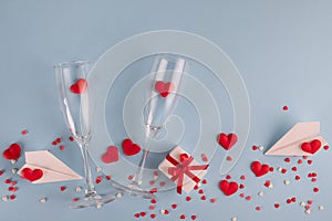 Valentine`s Day background. Gift box , alarm clock , red candy  hearts and paper plane, two champagne glasses on blue background