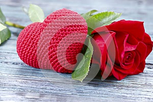 Valentine`s day background. On a gray wooden background in the center is a red knitted heart and a red rose.