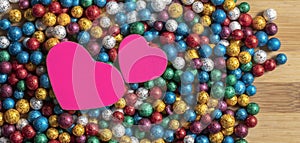 Valentine`s Day background. Multicolor small size thermocol decorative balls with two pink hearts on top of a wooden table