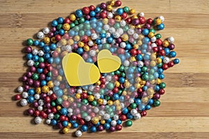 Valentine`s Day background. Multicolor small size thermocol decorative balls with two yellow hearts on top of a wooden table