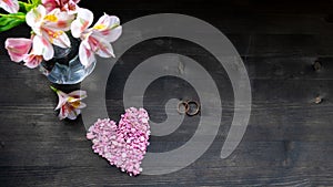 Valentine`s day background - pink heart, flowers, tablet and wedding rings on a dark background
