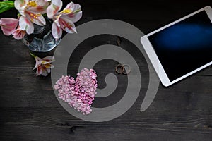 Valentine`s day background - pink heart, flowers, tablet and wedding rings on a dark background