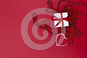 Valentine`s day background. On a red background on the right is a white gift box and red beads.