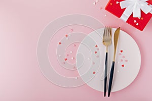 Valentine`s Day background. A set of golden cutlery and pink napkin on plate with hearts confetti
