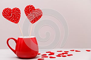 Valentine`s day background. Two candy hearts in a red Cup and a scattering of small hearts on a light gray background