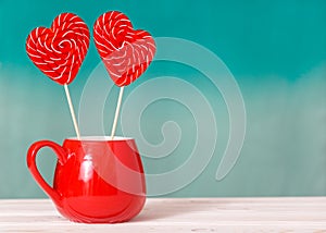 Valentine`s day background. Two heart shaped lollipops in a red Cup on a turquoise blue background. Concept on Valentine`s Day o