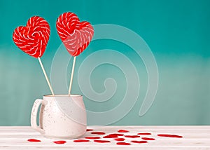 Valentine`s day background. Two lollipops-hearts in a white Cup on a turquoise background, scattering of hearts around