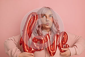 Valentine& x27;s Day banner with pretty young 20s woman having fun holding red foil love word balloons over pink