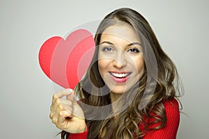 Valentine`s Day. Beautiful young woman in love holding a paper heart and smile at camera on gray background.