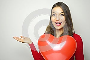 Valentine`s Day. Beautiful young woman wearing red dress and holding a red heart air balloon showing your product or text on whit