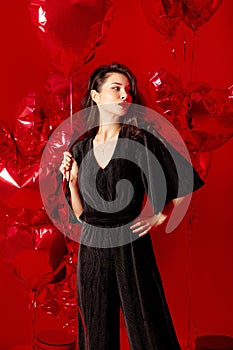 Valentine`s Day. Beauty girl in black with red heart-shaped balloons having fun