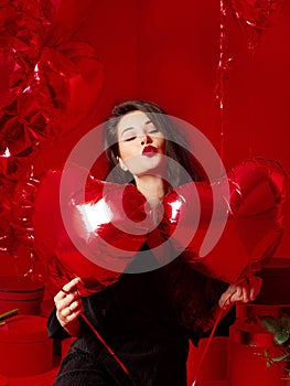 Valentine`s Day. Beauty girl in black with red heart-shaped balloons having fun