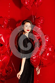 Valentine`s Day. Beauty girl in black with red heart-shaped balloons having fun