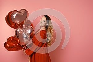 Valentine`s Day Beauty girl with red dress and pink air balloons. Happy young woman posing and laughing at the camera. Love