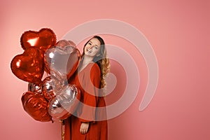Valentine`s Day Beauty girl with red dress and pink air balloons. Happy young woman posing and laughing at the camera. Love