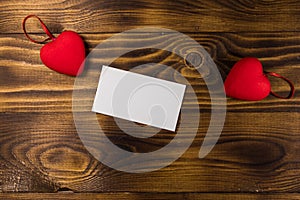 Valentine`s day blank greeting card and two red hearts on wooden background
