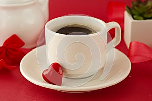 Valentine's Day breakfast. Cup of coffee over deep red background with red letter, decorative heart and plant. Top view