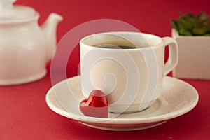 Valentine's Day breakfast. Cup of coffee over deep red background with red letter, decorative heart and plant. Top view