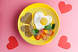 Valentine`s day breakfast. heart-shaped fried egg and bread in a yellow plate on a red background