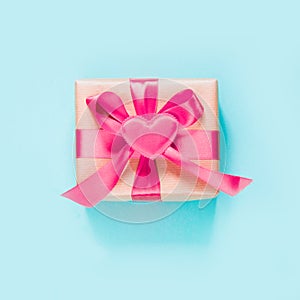 Valentine`s day card. Gift with pink ribbon and heart on blue surface. Top view. Square image.