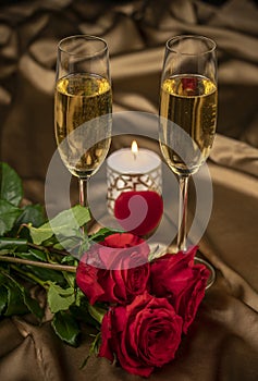 Valentine`s day card, two glasses of champagne on a gold background red roses and a red heart, a lighted candle