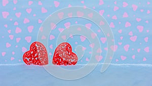 Valentine card with two red openwork hearts in a snowdrift on a blue background with pink hearts with space background