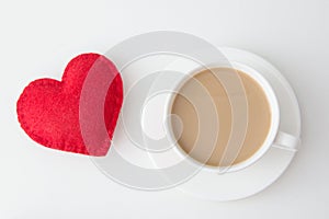 Valentine`s day card. White cup of hot coffee with milk and red felt heart on white. Top view.