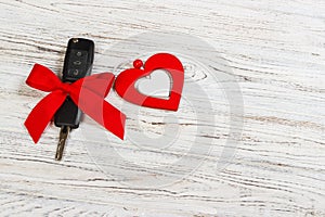 Valentine`s day or christmas car key gift. Car key with a red ribbon and heart on white wooden table