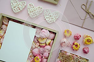 Valentine`s Day composition. Flat lay of white hearts, handmade gift boxes, craft paper, envelope, rose buds on pink background.