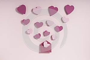 Valentine`s day composition. Pink and purple hearts blowing from envelope on pink background. Love message letter concept