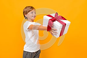 Valentine`s day concept. attractive boy holds out a box with a gift with a red ribbon on a bright yellow background