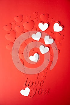 Valentine`s day concept. The background is red, the red hearts are cut out of paper. Words I love you
