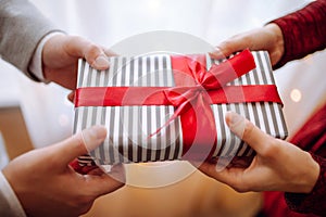 Valentine`s day concept. A giftbox with red ribbon in hands. Loving couple give each other presents on 14 February. Romantic