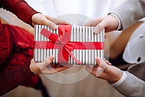 Valentine`s day concept. A giftbox with red ribbon in hands. Loving couple give each other presents on 14 February. Romantic