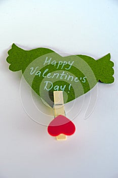 Valentine`s day concept. Green paper heart with wings and congratulation fixed on a clothespin on white background.