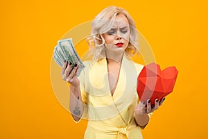Valentine`s day concept. portrait of a sexy blond girl with red lips with a red heart made of paper and money in hands