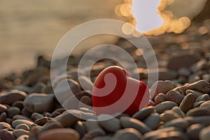Valentine's Day concept. Red heart romantic love symbol on pebble beach at sunset with copy space. Template for