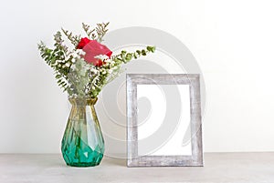 ValentineÃ¢â¬â¢s day concept, Red roses flower bouquet in glass vase and blank grey vintage wooden frame on table background with