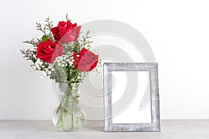 ValentineÃ¢â¬â¢s day concept, Red roses flower bouquet in glass vase and blank grey vintage wooden frame on table background with